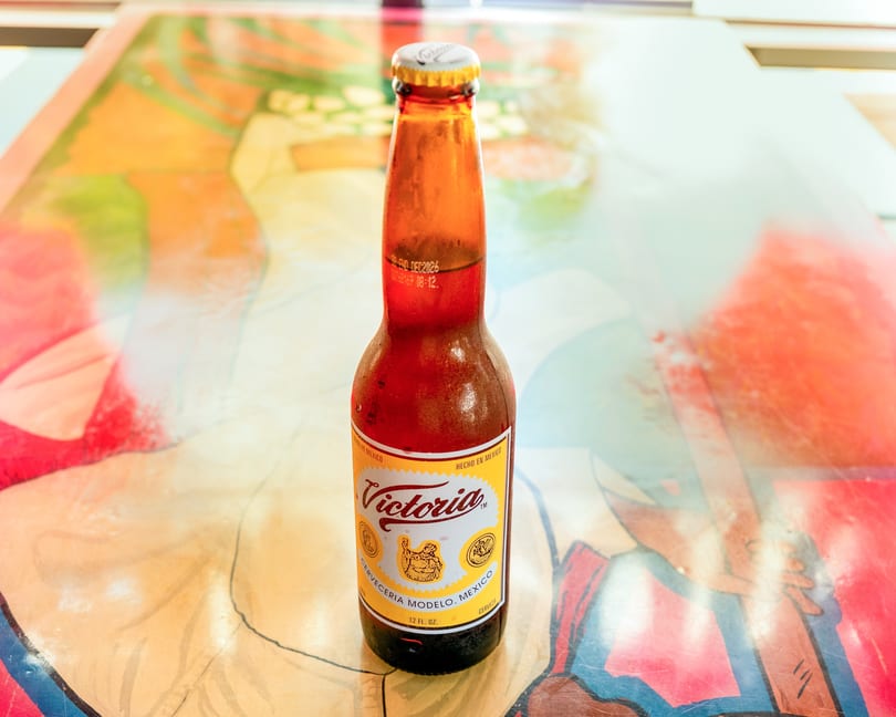 A cold bottle of Victoria beer with condensation, sitting on a colorful, abstract table.