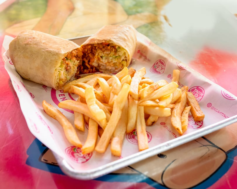 A large burrito, cut in half to show the filling, served with a side of golden french fries.