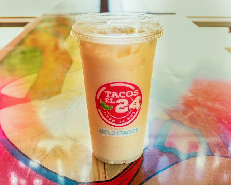 Iced horchata drink from Tacos El 24, with a red logo, on a colorful table.