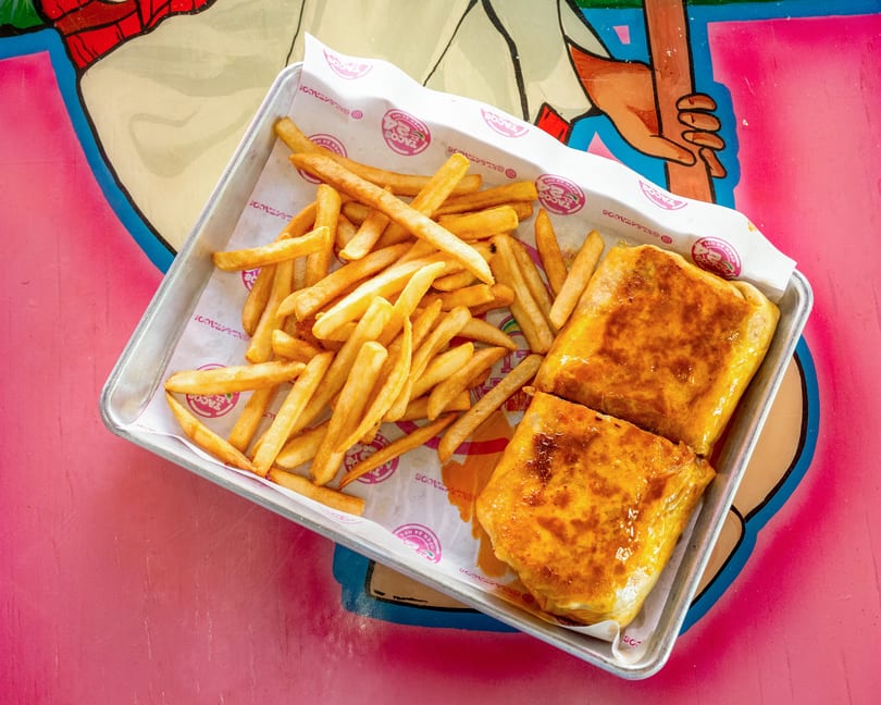 Two golden-brown burritos and a pile of crispy french fries on a metal tray with branded paper.