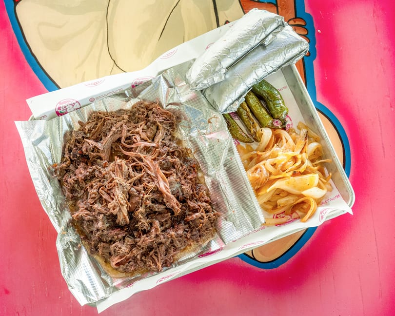 Shredded beef, grilled onions, and green peppers on a foil-lined tray, with two foil-wrapped items.